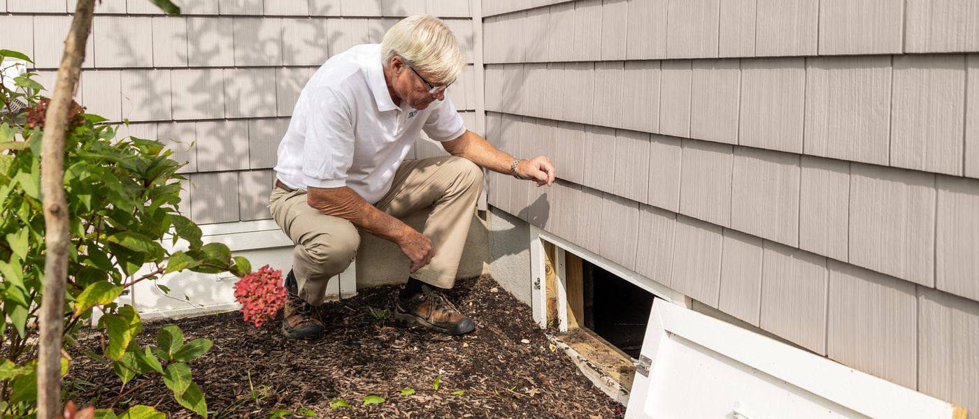 Radon specialist inspecting a crawl-space access opening beside a Cincinnati-area home